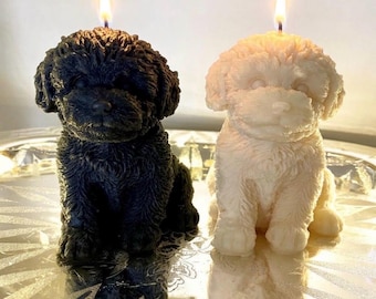 May include: Two sculpted candles shaped like sitting puppies, one in solid black and one in solid white. Each candle features a textured, curly fur design and a single lit wick centered on the top of the head, creating a warm glow.