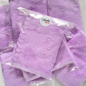 May include: A stack of lavender-colored microfiber cloths in clear plastic packaging. The packaging has a round sticker with the text "Nadia MLB" on it.