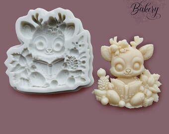 May include: A white silicone mold and a matching off-white molded figure of a deer reading a book, surrounded by poinsettia flowers and pinecones. The text My Little Bakery is visible in the upper right corner of the image.