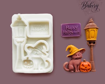 May include: A white silicone mold featuring cavities for a street lamp, a rectangular sign with the text Happy Halloween, a cat wearing a witch hat, and a pumpkin. Beside the mold are finished pieces in purple, yellow, brown, and orange.