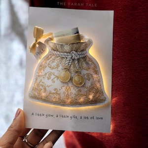 Op de afbeelding: Handgemaakte wenskaart met een geldbuidelontwerp, gouden details en een treklipje. De kaart heeft een gloeiend effect en de tekst luidt "A little glow, a little gift, a lot of love."