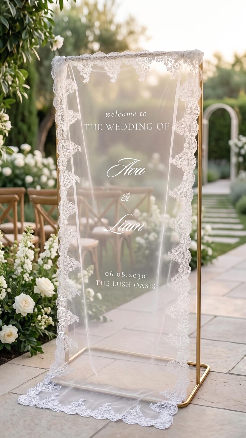 Pu&ograve; includere: Un alto telaio rettangolare in metallo dorato che sostiene un pannello in tessuto bianco trasparente, rifinito con un intricato bordo in pizzo bianco. Il testo stampato in bianco recita: welcome to THE WEDDING OF Ava & Liam 06.08.2030 THE LUSH OASIS.