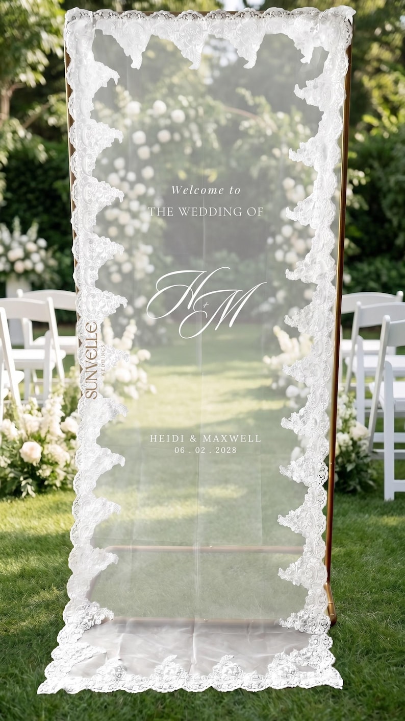 Pu&ograve; includere: Un cartello di benvenuto per matrimoni rettangolare e semitrasparente con bordo in pizzo bianco. Il testo recita: Welcome to THE WEDDING OF, il monogramma HM, HEIDI & MAXWELL e la data 06.02.2028. Il marchio SUNVELLE &egrave; stampato verticalmente.
