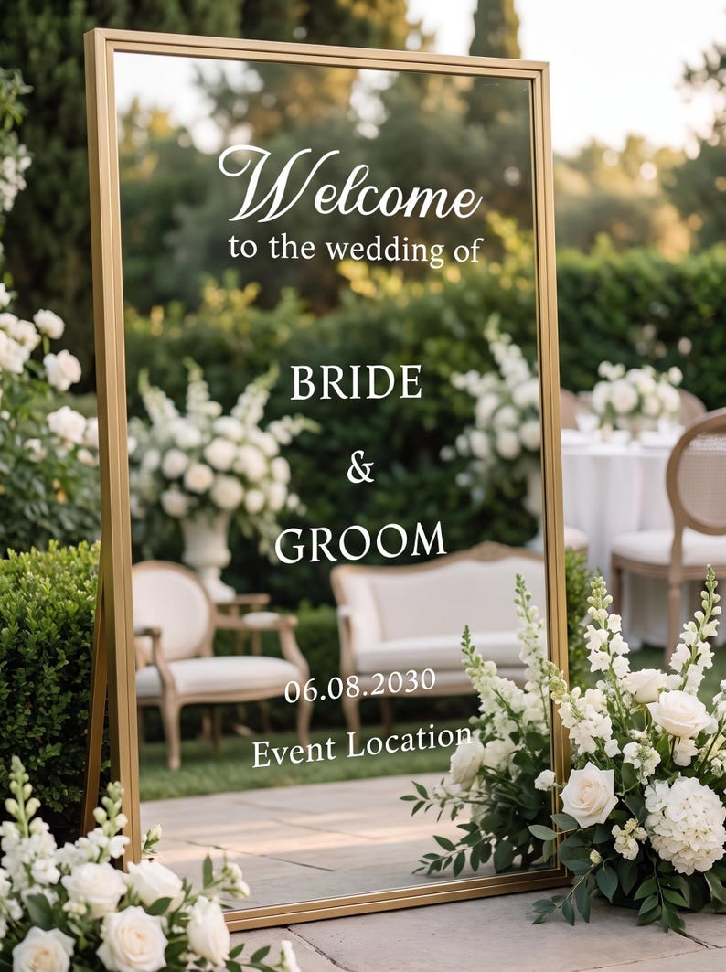 May include: A tall rectangular mirror with a gold frame featuring white text that reads Welcome to the wedding of BRIDE & GROOM 06.08.2030 Event Location. The mirror reflects a garden setting with white flowers and outdoor furniture.