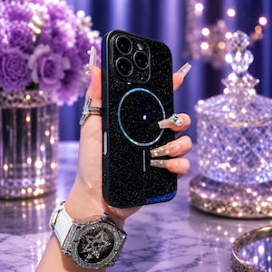 May include: A black glittery smartphone case featuring a circular magnetic charging ring design on the back. The case has a triple camera cutout at the top left corner and a vertical alignment line below the magnetic ring, showcasing a sleek finish.
