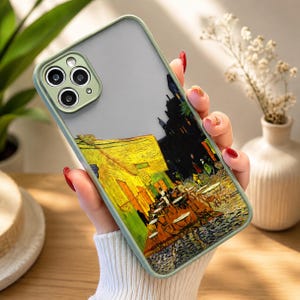 May include: A phone case with a matte sage green frame and a semi-transparent back panel featuring a printed reproduction of Vincent van Gogh's Cafe Terrace at Night painting, showcasing a yellow cafe building and a dark blue starry night sky.