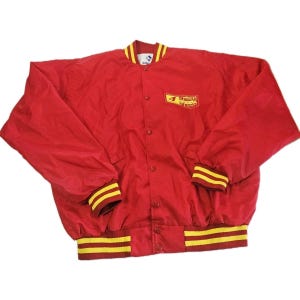 May include: A red nylon bomber jacket featuring a snap-button front closure, long sleeves, and ribbed cuffs and hem with yellow stripes. A yellow rectangular patch on the chest displays the text "Sheetz" in red lettering with a small logo above it.