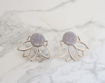 May include: A pair of silver earrings with a white glitter lotus flower design.