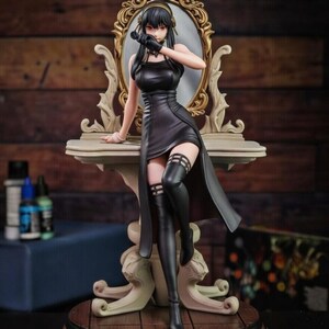 May include: A collectible anime-style figurine of a character with long black hair, wearing a black sleeveless dress and black thigh-high boots. The figure is posed sitting on a light-colored vanity table with an ornate gold-framed mirror behind it.