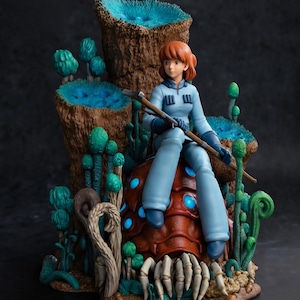 May include: A figurine of a person with reddish-brown hair wearing a light blue jumpsuit, holding a staff, and sitting on a brown, segmented creature with glowing blue spots, surrounded by tall brown structures with blue tops and green plants.