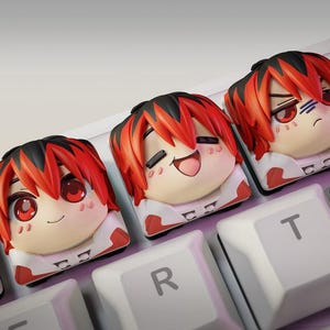Puede incluir: Tres teclas personalizadas para teclado mecánico con cabezas de personajes estilo anime esculpidas con cabello rojo y negro. Cada tecla muestra una expresión facial diferente, incluyendo una sonrisa suave, una risa alegre y una mirada seria.