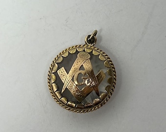 Puede incluir: Pendiente de oro con una cara de vidrio transparente que presenta un símbolo masónico de oro con una 'G' en el centro.
