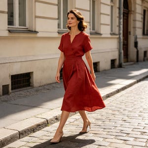 May include: A rust-colored midi dress featuring a V-neckline, short sleeves, and a wrap-style bodice with a defined waistline. The skirt is pleated and falls to a mid-calf length. The garment is paired with neutral-toned pointed-toe high heels.