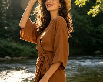 Puede incluir: Un vestido cruzado de color marrón con mangas anchas y un cinturón de lazo a juego en la cintura, combinado con un sombrero de paja de color tostado claro. El vestido presenta un escote en V y un acabado de tela texturizada muy sencillo.