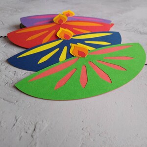 May include: Four colorful paper decorations in a row. Each is a half-circle shape with a flame design on top. The colors include green, blue, red, and purple. The flames are yellow, orange, and red.