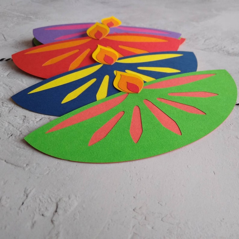 May include: Four colorful paper decorations in a row. Each is a half-circle shape with a flame design on top. The colors include green, blue, red, and purple. The flames are yellow, orange, and red.