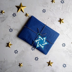 Closeup of gift wrap option.  Parcel is wrapped in dark blue tissue paper, tied with blue and white bakers twine withan electric blue and white star of david gift tag attached