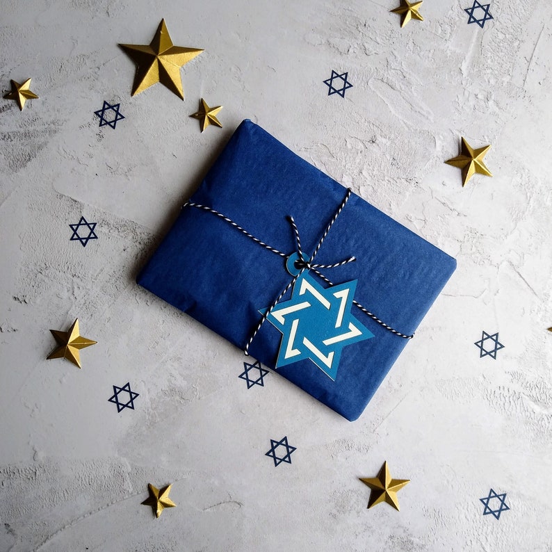 Closeup of gift wrap option.  Parcel is wrapped in dark blue tissue paper, tied with blue and white bakers twine withan electric blue and white star of david gift tag attached