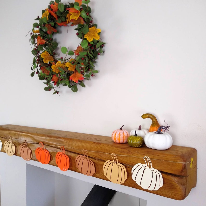 May include: A wooden mantelpiece decorated with a fall-themed garland of orange and yellow leaves. The garland is strung with paper cutouts of pumpkins in various shades of orange, yellow, and white.