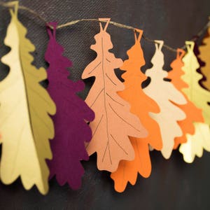 May include: A garland of paper oak leaves in various autumnal colors, including yellow, orange, red, and purple, strung together with twine.
