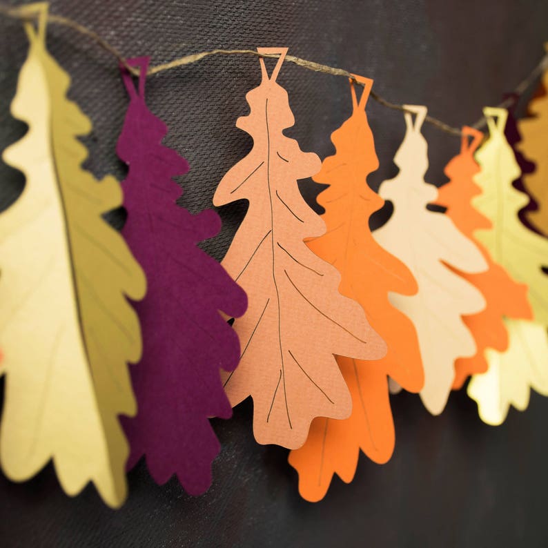 May include: A garland of paper oak leaves in various autumnal colors, including yellow, orange, red, and purple, strung together with twine.