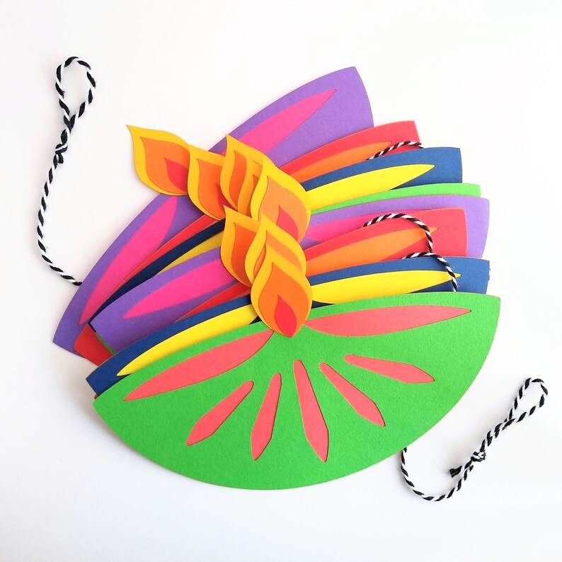 May include: A colorful paper craft resembling a stylized flame or flower. The design features layers of vibrant colors, including green, red, orange, yellow, purple, and blue. A black and white string is attached for hanging.
