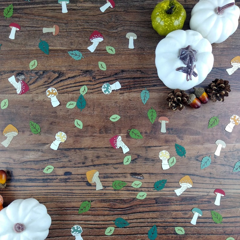 May include: A wooden background with a variety of fall-themed decorations, including mushrooms, leaves, and gourds. The mushrooms are in various colors, including red, white, and yellow. The leaves are green and brown. The gourds are white and green.