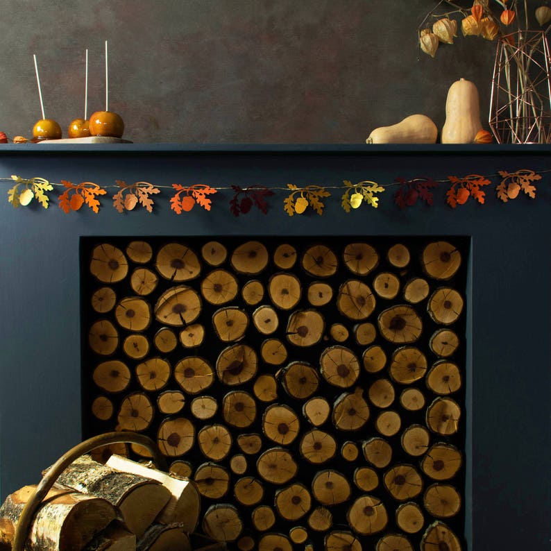 May include: A fireplace mantel decorated with a garland of fall leaves and acorns. The fireplace is filled with stacked logs of wood.
