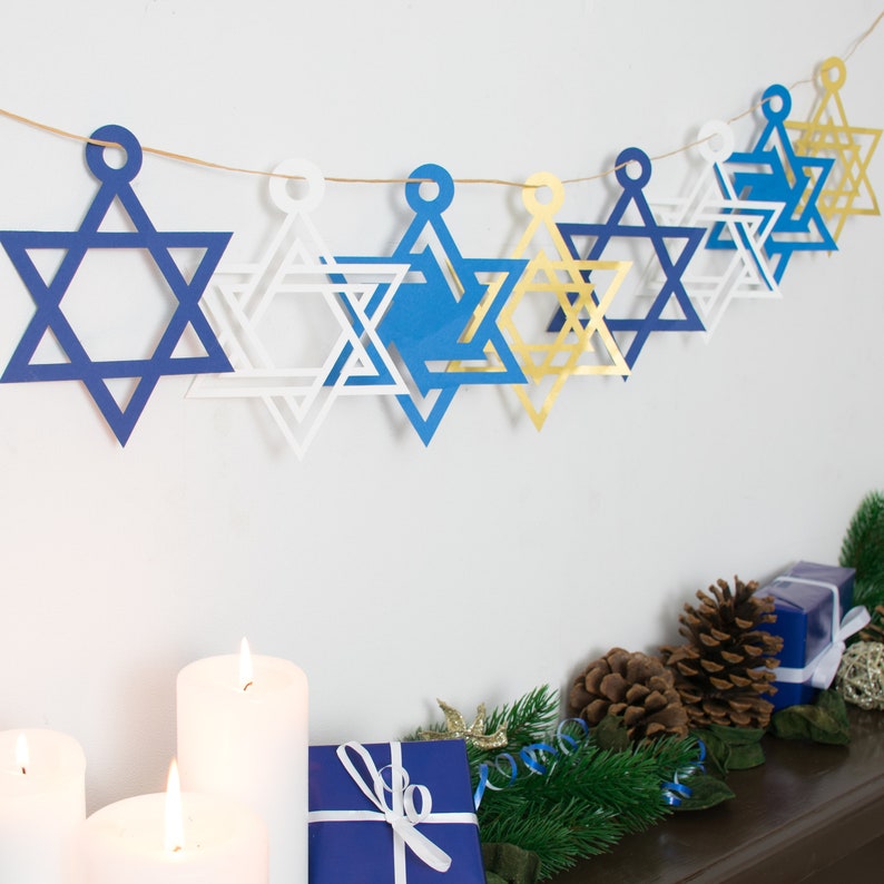 Closeup of small star of david garland hung on a white wall above a decorated mantelpiece