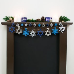 Large and small sized star of david garlands displayed together strung across a dark wood mantelpiece.  Stars are electric blue, white, navy blue and silver