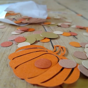 May include: Orange paper pumpkin cutout with brown and orange paper circles scattered around it.