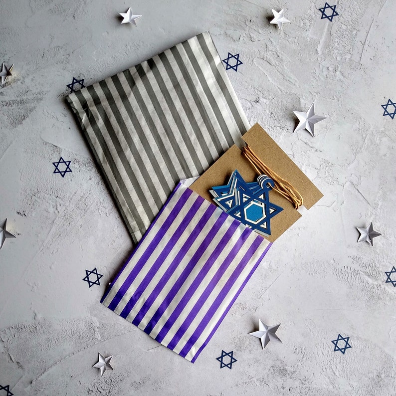 Closeup of Standard packaging option.  Large garland is wrapped in grey and white  vertically striped paper bag.  Small silver option star garland is shown slightly pulled out of blue and white vertically striped paper bag.