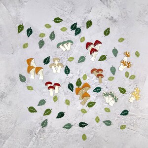 May include: A collection of colorful mushroom-shaped paper cutouts on a white textured background. The mushrooms are in various shades of red, orange, yellow, and green.