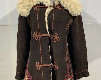 May include: A brown suede coat with a faux fur collar and embroidered floral details. The coat has a long, fitted silhouette and features a button closure.