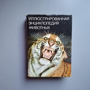 以下が含まれることがあります： 「ИЛЛЮСТРИРОВАННАЯ ЭНЦИКЛОПЕДИЯ ЖИВОТНЫХ」というタイトルのハードカバー本。表紙の上部には、口を開けて歯と舌を見せているトラの大きく詳細なカラー写真が、黒い背景をバックに配置されています。