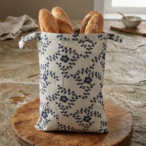 Könnte beinhalten: Eine beige Brottasche mit marineblauem Blumenmuster, die drei Brote enthält. Die Tasche hat einen weißen Kunststoffverschluss und steht auf einem Holzschneidebrett. Das Brot ist goldbraun.