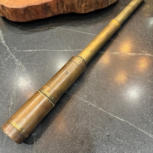Peut inclure: Une longue lunette astronomique cylindrique en laiton avec une finition métallique patinée. Cet instrument optique portatif présente plusieurs sections télescopiques, une extrémité à objectif large et un oculaire plus petit à l'autre extrémité.