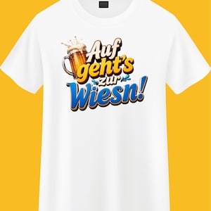May include: A white short-sleeved t-shirt featuring a graphic of a beer mug with foam and the text "Auf geht's zur Wiesn!" in bold, stylized yellow and blue lettering. The design is centered on the chest of the shirt, which has a crew neckline.