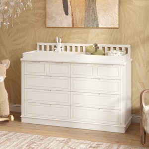 May include: A white wooden dresser featuring eight drawers arranged in two columns, topped with a removable changing tray. The tray holds a small white plush rabbit, a green dinosaur toy, and a patterned container. The dresser has a slatted back.