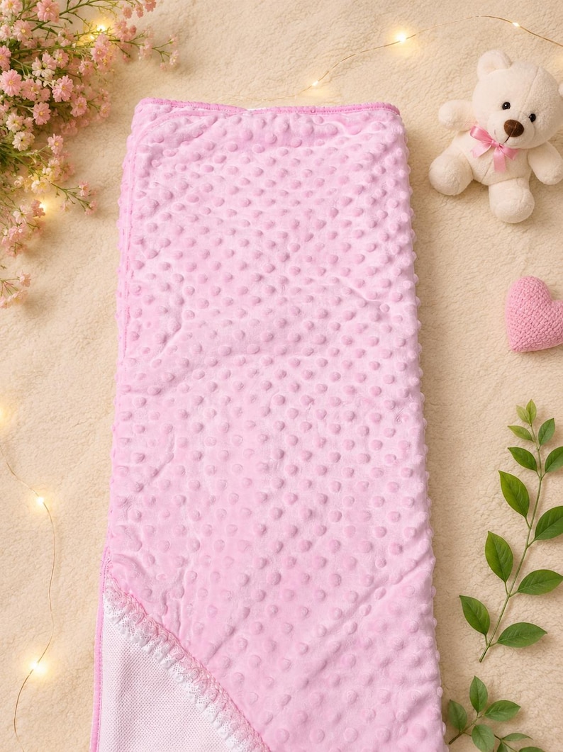 May include: A rectangular baby blanket featuring a soft light pink minky fabric with a raised dimple texture. The blanket has a folded corner revealing a white mesh lining and a decorative white lace trim along the edge of the fabric fold.