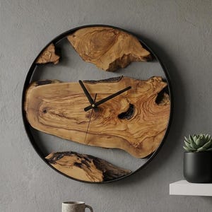 May include: A circular wall clock featuring a black metal frame surrounding natural live-edge wood slices with visible grain and knots. The clock face includes thin black hour, minute, and second hands positioned in the centre of the wood pieces.