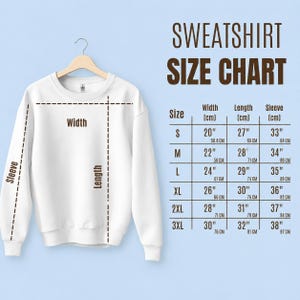 May include: A white sweatshirt hanging on a wooden hanger, with a size chart displayed to the right. The chart shows measurements for width, length, and sleeve length in inches and centimeters for sizes S through 3XL.