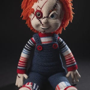 May include: Crocheted doll resembling Chucky, the horror movie character. The doll has orange yarn hair, a stitched face, and wears blue overalls with red buttons. The arms and legs have striped patterns in red, white, and blue.