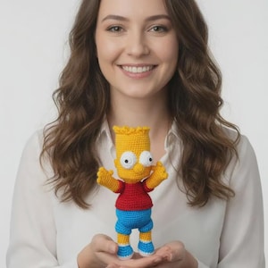 May include: A handmade crochet doll of Bart Simpson, featuring a yellow head, red shirt, blue shorts, and white and blue shoes. The doll has large eyes and is posed with arms outstretched. The doll is held in front of a white background.