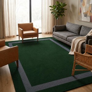 May include: A rectangular area rug featuring a deep forest green center field enclosed by a wide, solid charcoal gray border. The rug has a low-pile texture and is positioned flat on a light-toned wooden floor, serving as a central floor covering.