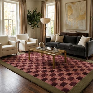 May include: A rectangular area rug featuring a repeating geometric checkerboard pattern in shades of deep burgundy and muted pink, framed by a solid olive green border. The rug is positioned on a dark wood floor in a living room setting.