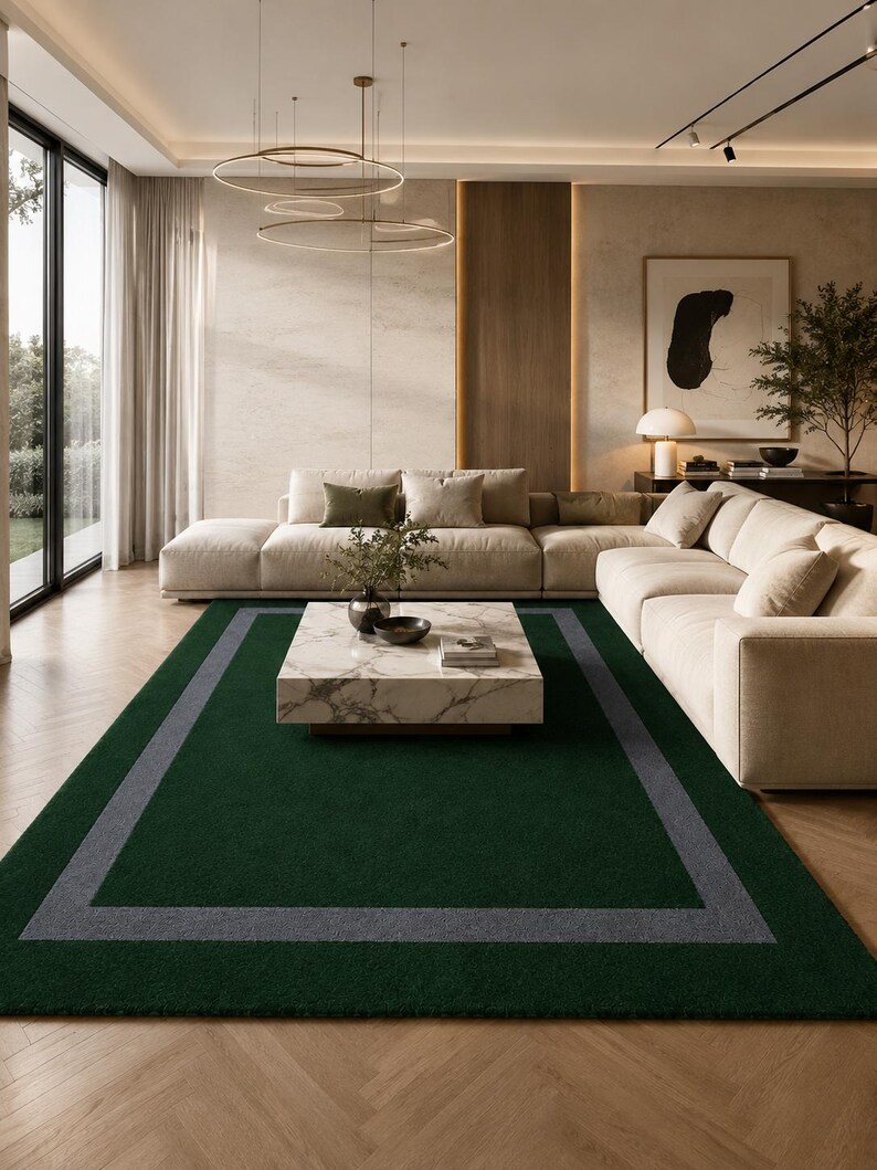May include: A rectangular area rug featuring a deep forest green center field bordered by a wide, solid gray frame. The rug has a short, dense pile texture and is positioned on a light-toned wooden floor with a herringbone pattern in a room.