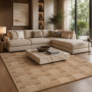 Peut inclure: Un grand tapis rectangulaire pr&eacute;sentant un motif g&eacute;om&eacute;trique de carr&eacute;s beiges et fauves entrelac&eacute;s. Le tapis est pos&eacute; sur un sol en bois devant un grand canap&eacute; d'angle beige, une table basse carr&eacute;e en marbre et un mur lambriss&eacute; en bois.