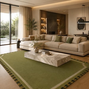 May include: A rectangular area rug featuring a solid olive green center, a light beige border, and an outer edge with a dark green and black checkered pattern. The rug is positioned on a light wood floor in front of a large beige sectional sofa.