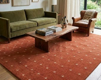 Peut inclure: Salon avec un tapis rouille à motif quadrillé de croix blanches. La pièce comprend un canapé vert, une table basse en bois et un fauteuil en cuir. Des œuvres d'art sont accrochées au mur.